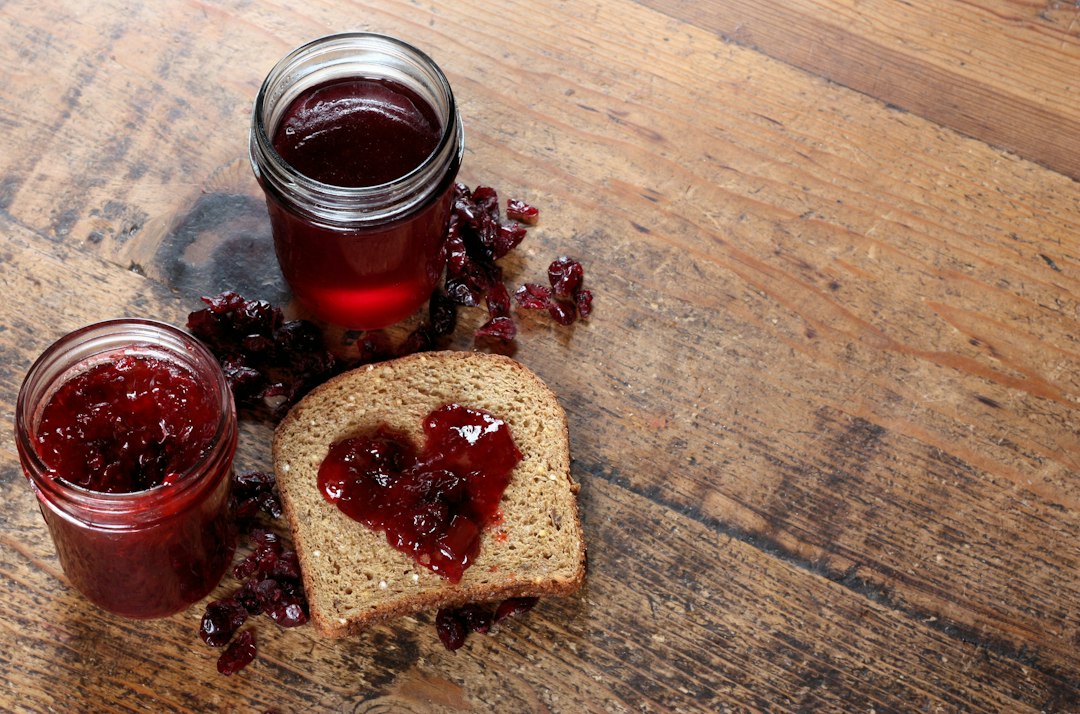 Two jars of jam sit next to a piece of bread